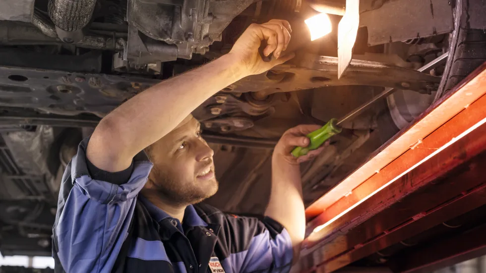 De automonteur kijkt onder de auto met een zaklamp